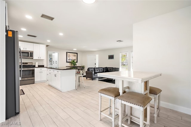 kitchen with white cabinets, a kitchen bar, stainless steel appliances, and light hardwood / wood-style flooring