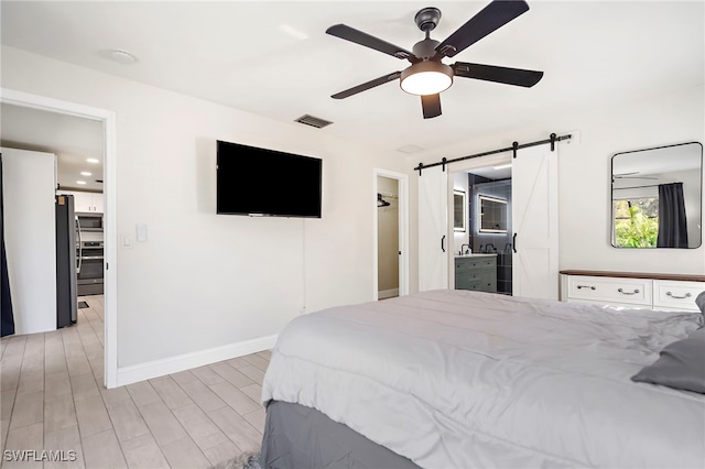 bedroom featuring ceiling fan, stainless steel fridge, a barn door, a spacious closet, and light hardwood / wood-style floors