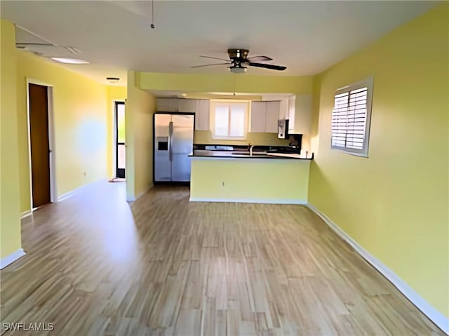 kitchen featuring a peninsula, white cabinetry, stainless steel refrigerator with ice dispenser, light wood finished floors, and dark countertops