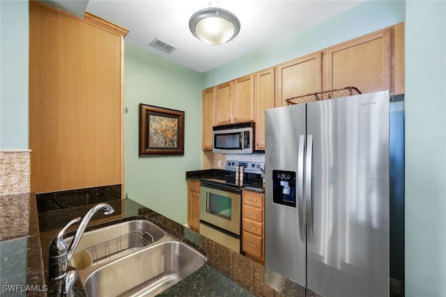 kitchen with backsplash, sink, dark stone countertops, light brown cabinetry, and stainless steel appliances