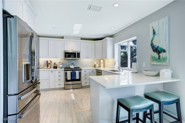 kitchen with white cabinets, sink, appliances with stainless steel finishes, kitchen peninsula, and a breakfast bar area