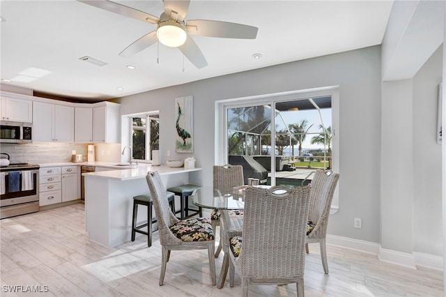 dining space with ceiling fan, light wood-type flooring, and sink