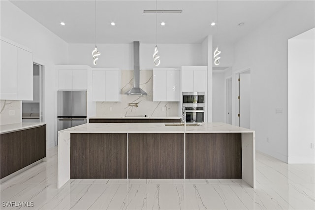 kitchen with a kitchen island with sink, white cabinets, hanging light fixtures, and wall chimney range hood