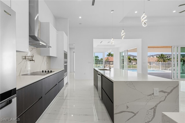 kitchen with a spacious island, white cabinetry, pendant lighting, and wall chimney range hood