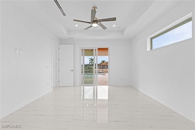 empty room with a raised ceiling, ceiling fan, and a healthy amount of sunlight