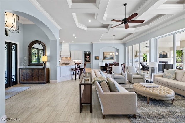 living room featuring coffered ceiling, ceiling fan with notable chandelier, ornamental molding, beam ceiling, and light hardwood / wood-style floors