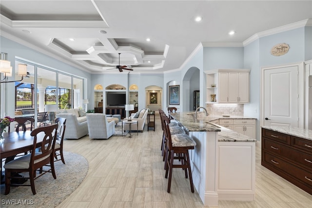 kitchen with a breakfast bar area, ceiling fan, light stone counters, and ornamental molding