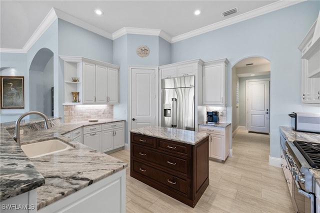 kitchen featuring light stone counters, crown molding, sink, high quality appliances, and white cabinetry