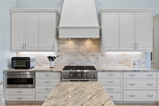 kitchen with white cabinets, decorative backsplash, appliances with stainless steel finishes, and custom exhaust hood