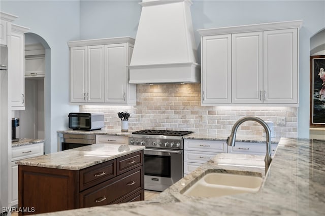 kitchen featuring premium range hood, sink, high end stainless steel range, light stone countertops, and dark brown cabinetry