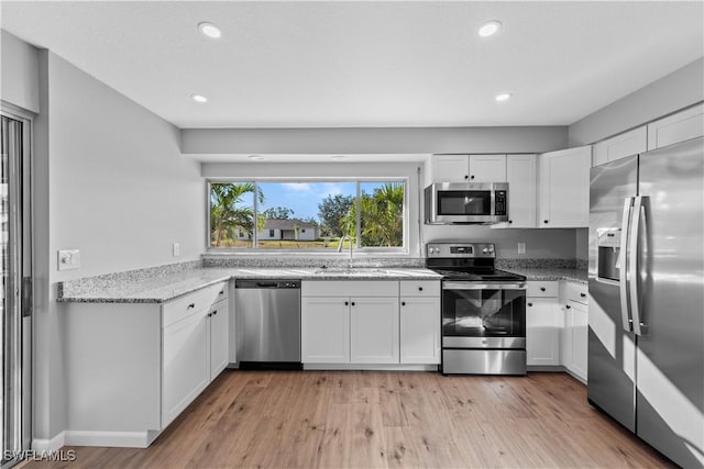 kitchen with light stone countertops, white cabinetry, sink, light hardwood / wood-style flooring, and appliances with stainless steel finishes