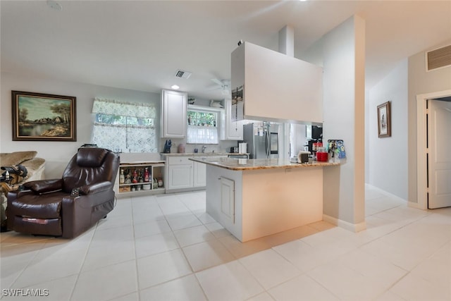 kitchen with kitchen peninsula, stainless steel fridge, light stone counters, white cabinets, and light tile patterned flooring