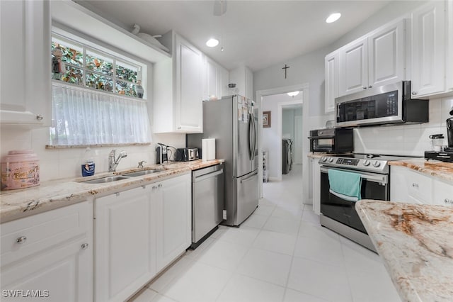 kitchen featuring light stone countertops, backsplash, stainless steel appliances, sink, and white cabinetry