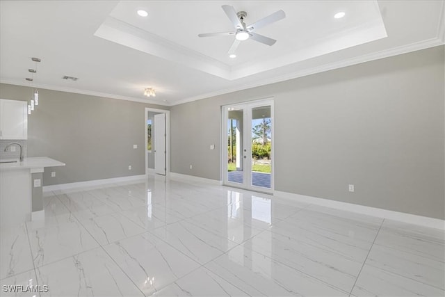 empty room with a tray ceiling, french doors, crown molding, a sink, and baseboards