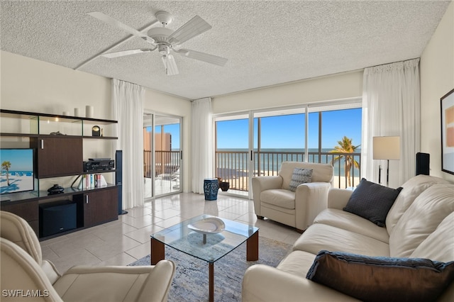 living room featuring ceiling fan, a water view, and a textured ceiling