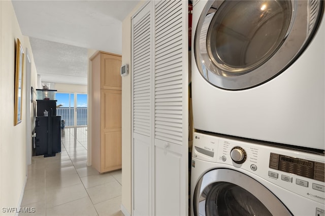 laundry room with a textured ceiling, light tile patterned floors, and stacked washer / dryer