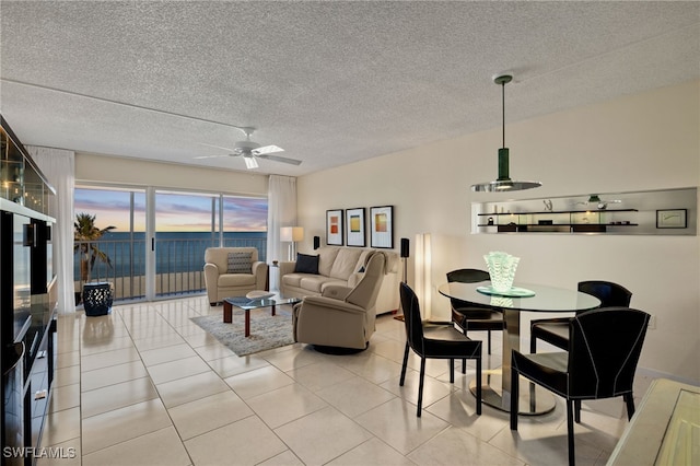 living room with light tile patterned floors, a textured ceiling, a water view, and ceiling fan