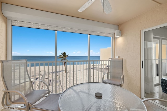 sunroom with ceiling fan, a water view, and a beach view