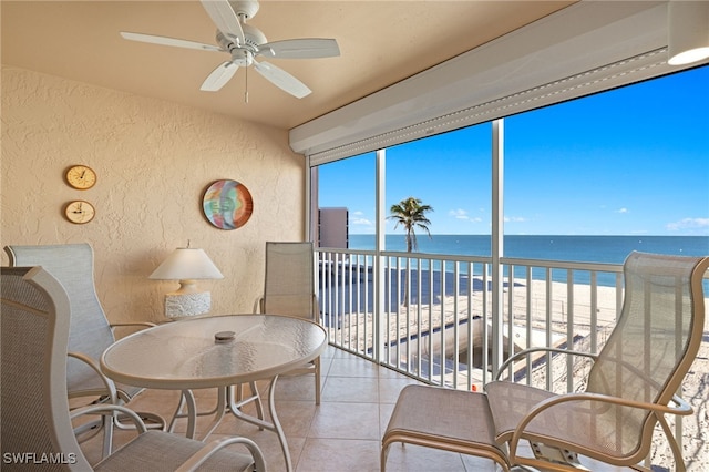 sunroom with ceiling fan, a water view, and a beach view