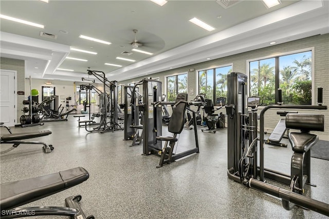 gym with a wealth of natural light, ceiling fan, and brick wall