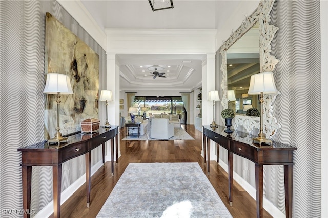 corridor with a tray ceiling, hardwood / wood-style flooring, and ornamental molding