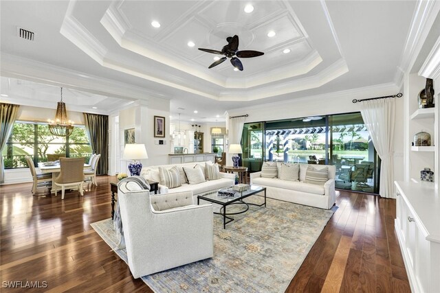 living room with dark wood-type flooring, ceiling fan with notable chandelier, a tray ceiling, and ornamental molding