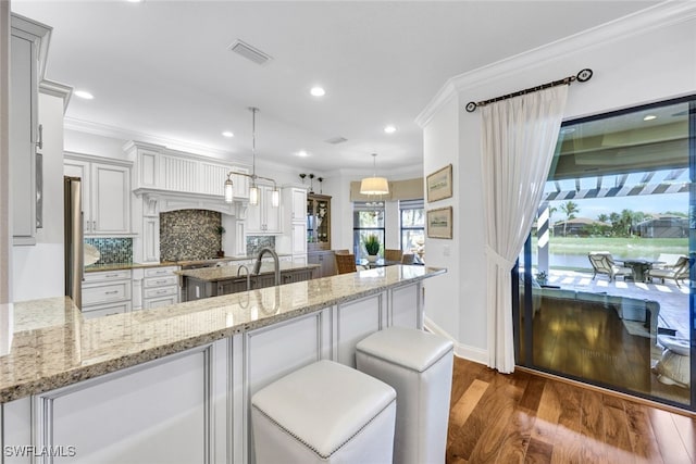 kitchen with pendant lighting, crown molding, a kitchen breakfast bar, tasteful backsplash, and light stone countertops