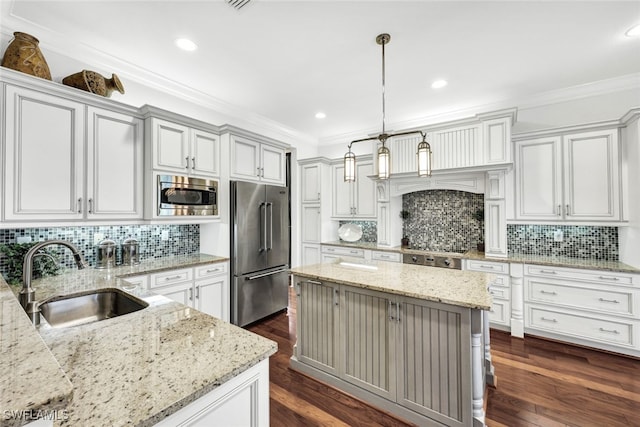 kitchen featuring sink, decorative light fixtures, appliances with stainless steel finishes, a kitchen island, and light stone countertops