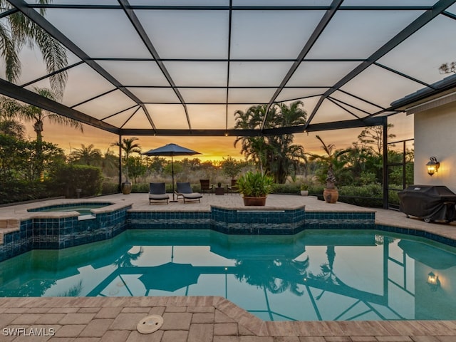 pool at dusk featuring glass enclosure, area for grilling, a patio area, and an in ground hot tub