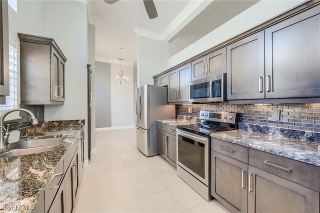 kitchen with dark stone counters, ornamental molding, stainless steel appliances, sink, and decorative light fixtures