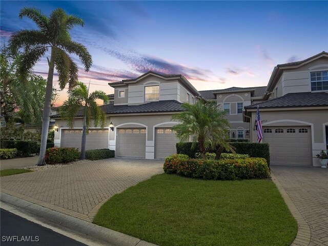 view of front of house with decorative driveway, a lawn, an attached garage, and stucco siding