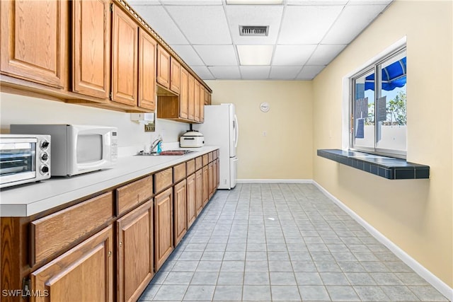 kitchen featuring a paneled ceiling, light tile patterned flooring, white appliances, and sink