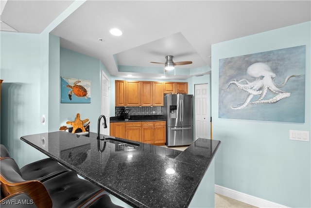 kitchen featuring a breakfast bar area, dark stone countertops, stainless steel fridge, and a raised ceiling