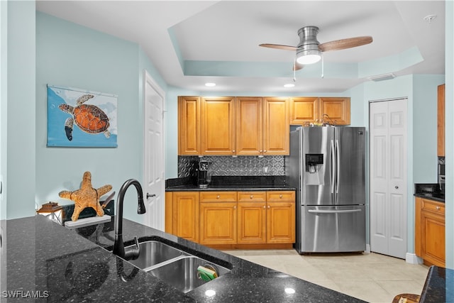 kitchen featuring dark stone counters, sink, stainless steel fridge, a tray ceiling, and tasteful backsplash