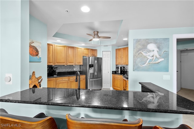 kitchen with ceiling fan, tasteful backsplash, stainless steel fridge with ice dispenser, a tray ceiling, and a kitchen bar