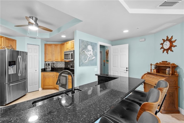 kitchen with backsplash, sink, dark stone countertops, appliances with stainless steel finishes, and a kitchen bar