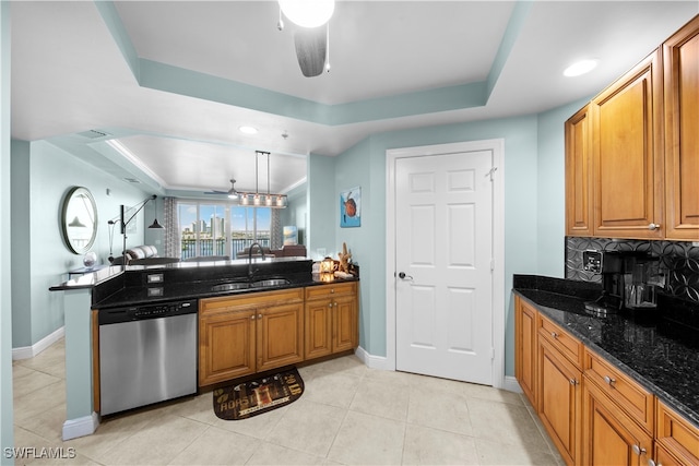 kitchen featuring dishwasher, sink, hanging light fixtures, a raised ceiling, and dark stone countertops