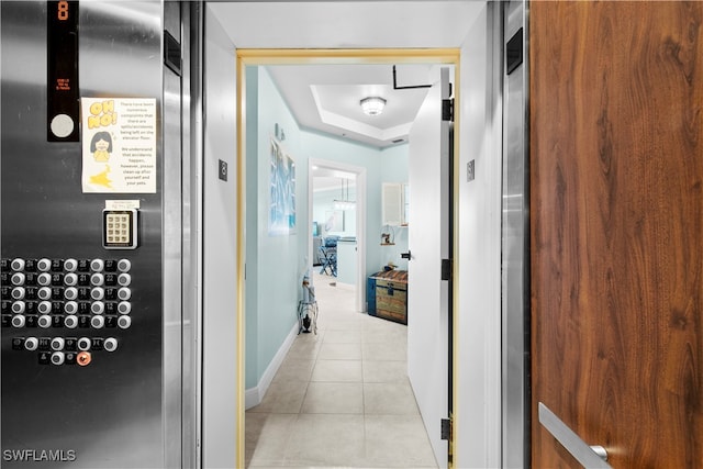 hall with light tile patterned floors and a tray ceiling