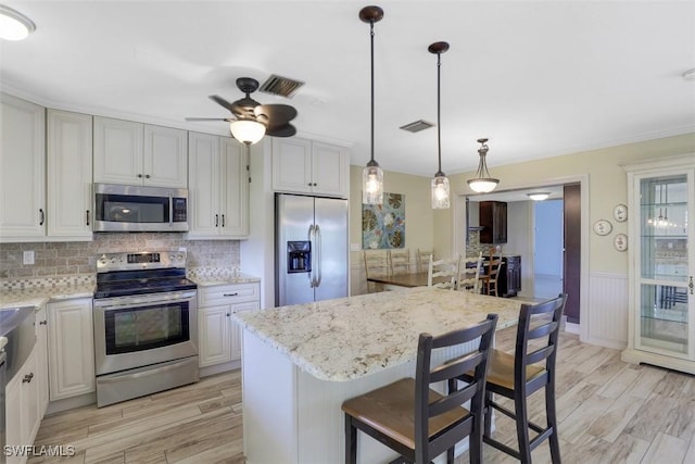 kitchen featuring a breakfast bar area, light stone counters, a center island, hanging light fixtures, and appliances with stainless steel finishes