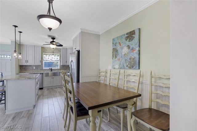 dining area featuring ceiling fan, light wood-style flooring, ornamental molding, and wainscoting