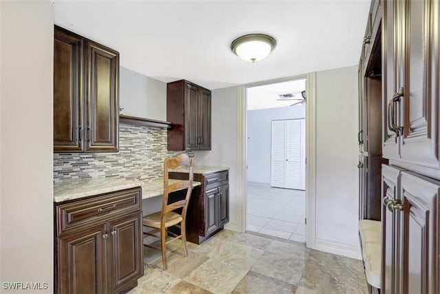 kitchen featuring light stone counters, backsplash, built in desk, and dark brown cabinetry