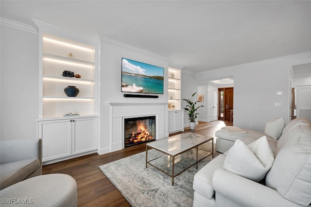 living area featuring crown molding, built in shelves, dark wood-type flooring, and a glass covered fireplace