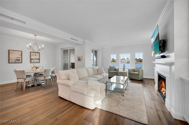 living room with baseboards, a glass covered fireplace, ornamental molding, wood finished floors, and a notable chandelier