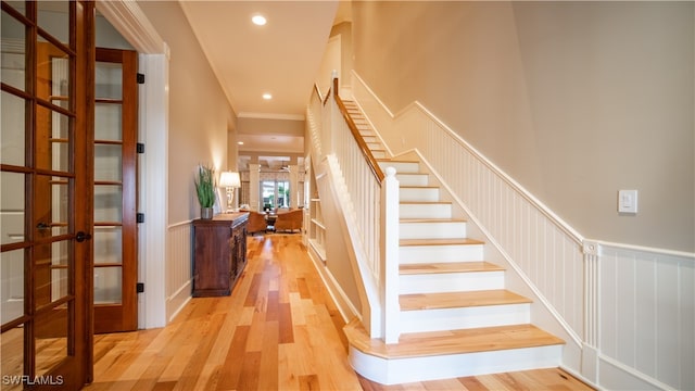 staircase featuring wood-type flooring, ornamental molding, and french doors