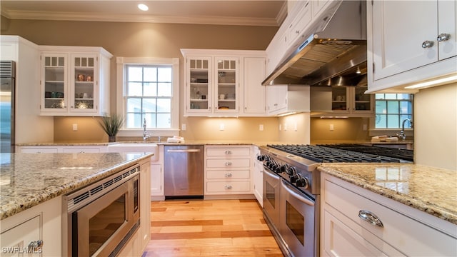 kitchen featuring light stone counters, light hardwood / wood-style flooring, ventilation hood, white cabinets, and high end appliances