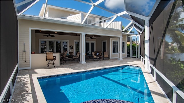 view of swimming pool featuring ceiling fan, a patio area, exterior bar, and glass enclosure