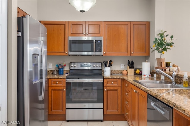 kitchen with light tile patterned flooring, appliances with stainless steel finishes, light stone counters, and sink