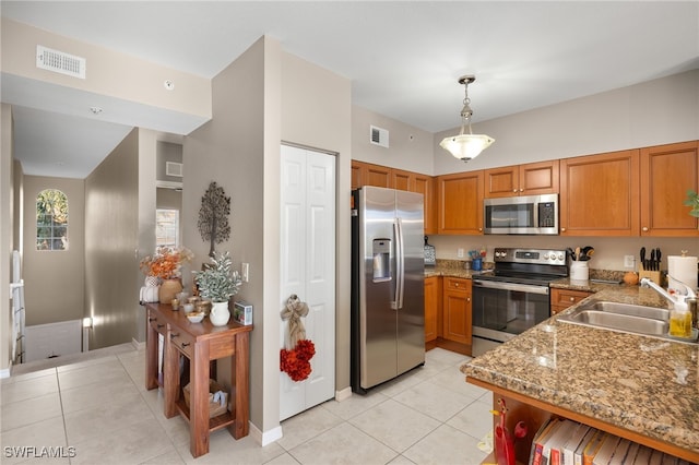 kitchen with stainless steel appliances, sink, light tile patterned floors, stone counters, and hanging light fixtures