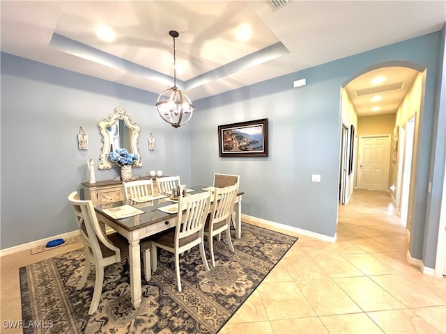 tiled dining area featuring a raised ceiling and a chandelier