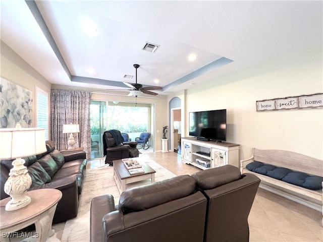 living room featuring a tray ceiling, ceiling fan, and light tile patterned flooring